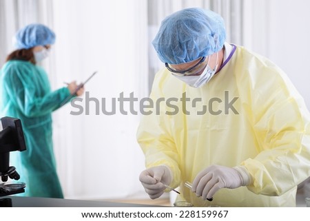 two scientist or doctors in protective gear working with microscope and blood, in lab or hospital