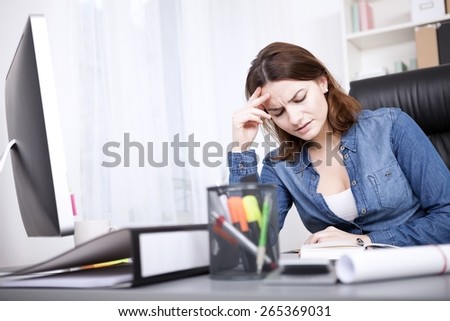 Close up Worried Young Businesswoman in Denim Blouse Sitting at her Office Table in the Office with Hand on her Forehead and Closed Eyes.
