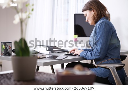 Busy Pretty Young Businesswoman in Denim Blouse Sitting at her Worktable with Documents and Electronic Devices.