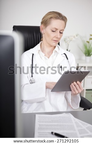 Serious Adult Woman Doctor Browsing at her Tablet Computer While Sitting at her Worktable