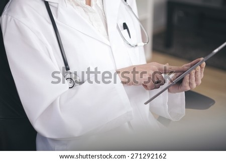 Close up Medical Doctor in White Suit with Stethoscope Busy Browsing at her Tablet Computer.