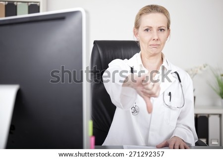 Upset Female Doctor Sitting at her Office, Showing Conceptual Thumbs Down Sign While Looking at the Camera.