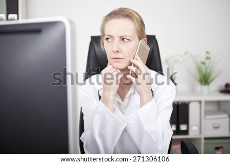 Adult Woman Physician Sitting at her Office While Calling Over the Mobile Phone and Looking to the Left Seriously While Leaning on One Hand.