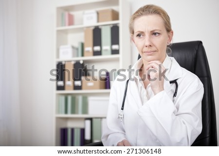 Close up Pensive Adult Female Doctor Sitting at her Office and Looking Afar with One Hand on her Chin