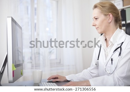 Serious Female Doctor Sitting at her Desk Checking Some Information Through Internet. Captured in Side View.