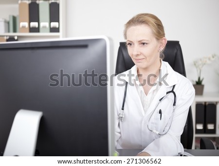 Serious Female Physician with Stethoscope on her Shoulders Looking at the Computer Monitor on her Table While Checking Some Information.