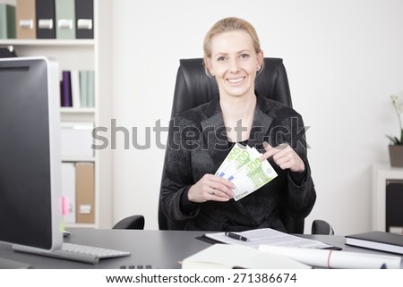 Smiling Blond Manageress in Black Business Attire Holding a Fan of Cash While Sitting at her Office and Looking at the Camera.