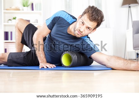 Gorgeous Athletic Young Guy Using Foam Roller in Doing an Indoor Exercise While Looking at You.