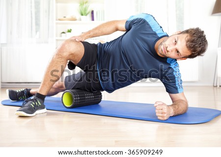 Handsome Athletic Young Man Doing Side Planking with Foam Roller on his Thigh.