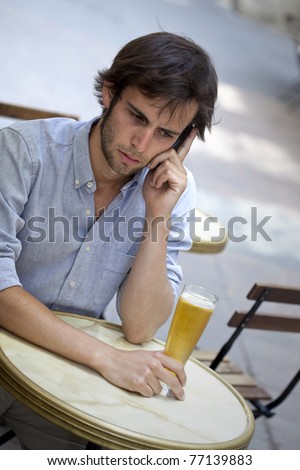 Youg man with a cell phone, drinking a beer on a cafe terrace