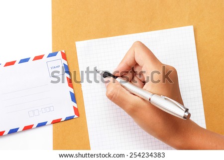Female hand writing a letter on paper with envelope on the table view 1