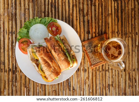 Natural light photo of chicken baguette on plate with glass of beer on mat on bamboo table top view
