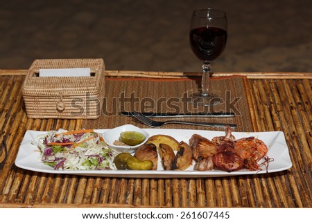 Natural light photo with shallow DOF of seafood mix barbecue with salad and glass of wine on plate on bamboo table view 2