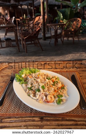 Fried rice with seafood on white plate on bamboo table with seaside cafe view 1