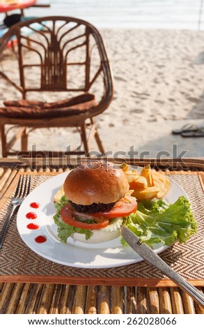 Natural light photo with shallow depth of field of chicken burger and french fries on plate and mat with tableware in beach cafe view 3