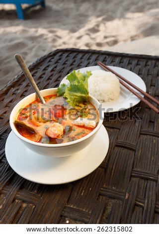 Natural light photo of Tom Yam seafood soup served with rice, shallow DOF seaside view 1