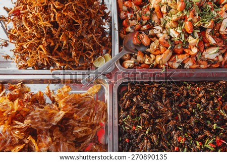 Street photo of asian market food in Cambodia. Top view of crab claws, frogs, fish, locust