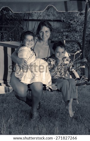 Retro style special toned photo of children and their mother in the summer garden hugging on a swing