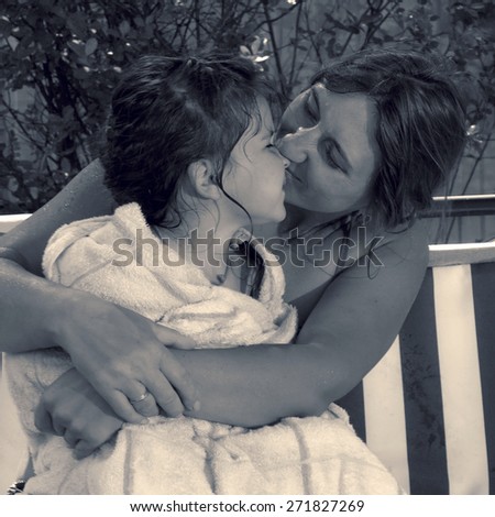 Retro style special toned photo of little girl and her mother in the summer garden hugging and kissing on a swing