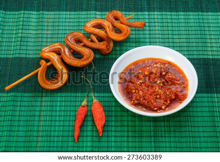Grilled snake on skewer with chili sauce on white plate on green mat side view 1