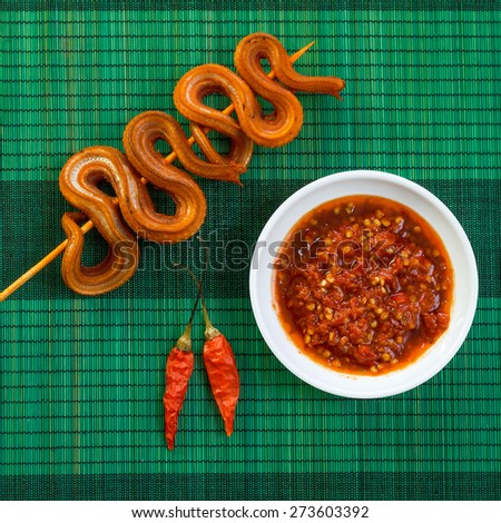 Grilled snake on skewer with chili sauce on white plate on green mat top view
