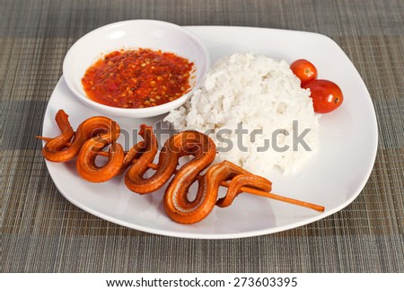 Grilled snake on skewer with chili sauce and steamed rice on white plate on mat side view