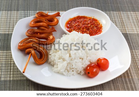 Grilled snake on skewer with chili sauce and steamed rice on white plate on mat side view 2