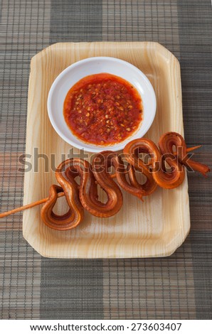 Grilled snake on skewer with chili sauce on white plate on mat top view 2