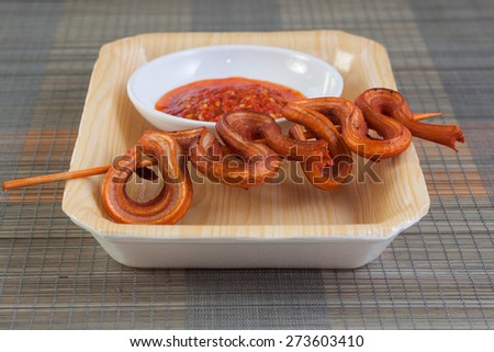 Grilled snake on skewer with chili sauce on white plate on mat side view