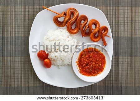 Grilled snake on skewer with chili sauce and steamed rice on white plate on mat top view