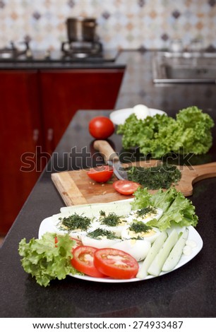 Assorted vegetables and eggs with a chopping board and a knife on granite surface with kitchen at background