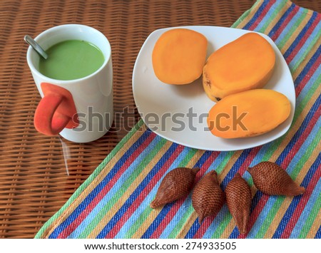 Cup of green tea with milk and with tropical fruits on a glass surface