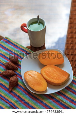 Cup of green tea with milk and with tropical fruits on a glass surface with reflection of sky
