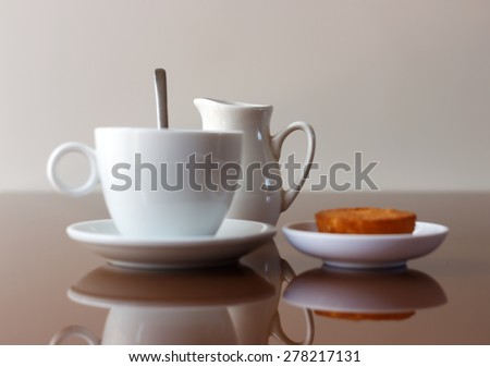 Cup of coffee, creamer jug and muffin on reflective table, side view with selective focus