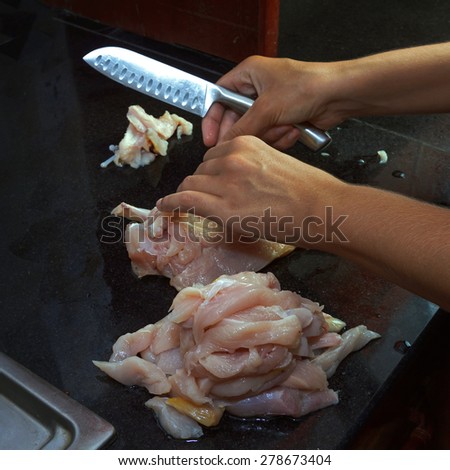 Female hands cutting raw chicken breast on black granite table. Selective focus