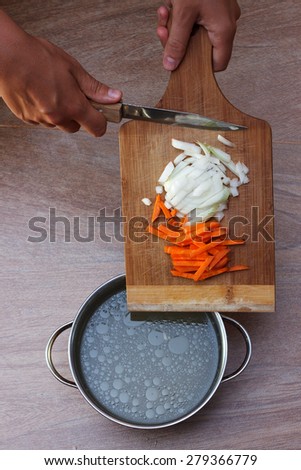 Female hands putting fresh vegetables ingredients into chicken soup, top view 1