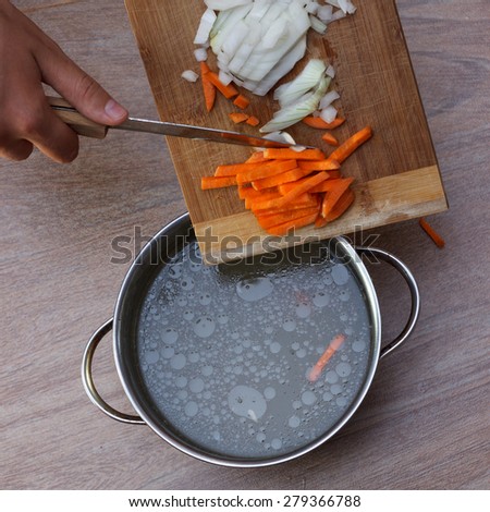 Female hands putting fresh vegetables ingredients into chicken soup, top view 2