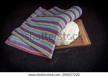 Closeup of pastry dough on baking board on black marble table covered by a dish-cloth view 1