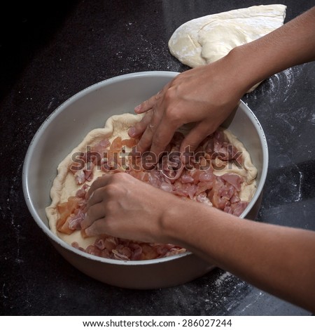 Closeup of a chicken and potato pie cooking process, hands filling a pie in a baking dish on black marble table, view 1