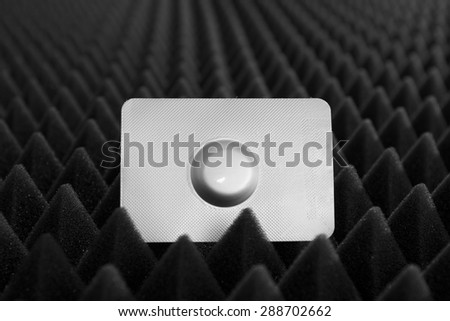 One medical pill in blister pack against black bumpy background, view 6