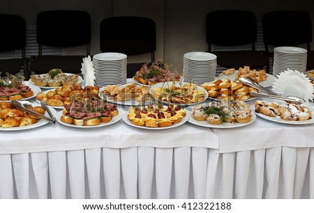 Catering banquet table with baked food snacks, sandwiches, cakes, cups and plates, self serve, open buffet dinner, horizontal view