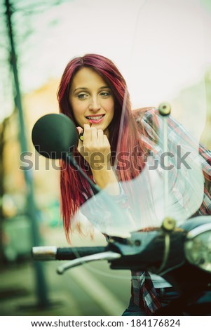 Young beautiful woman on motorcycle fixing her make up.