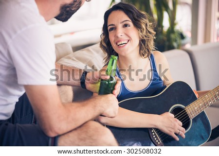Young couple sitting on a couch with a guitar. The girl is playing the guitar.