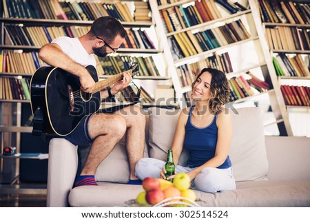 Young couple sitting on a couch with a guitar. The man is playing the guitar.