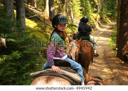 Young girl horseback riding along forest trail.