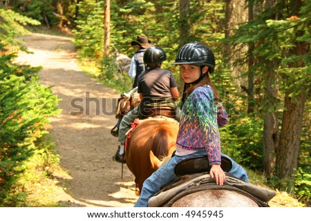 Young girl horseback riding along forest trail.