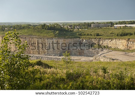 View down into a rock quarry surrounded by green hills, trees and commercial buildings