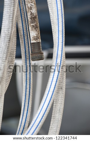 A garden hose displays the contrast between the pristine white and blue striped loop of the hose that is clean with the filthy, dirt embedded nozzle end