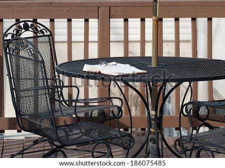 A pair of reading glasses rests on top of an open Bible on a wrought-iron patio table on a wooden deck as the evening shadows settle in.