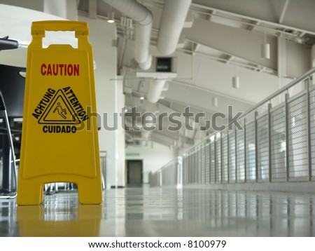 Sign saying caution in English and Spanish, with a view of a long, empty, industrial-looking corridor